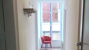 A hallway with a red chair, a decorative shelf, and a large window with a view of the outside.