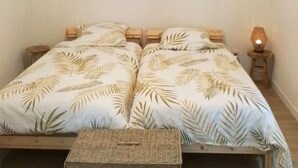 A bedroom with a double bed, two bedside tables, a small bedside lamp, and a woven stool.