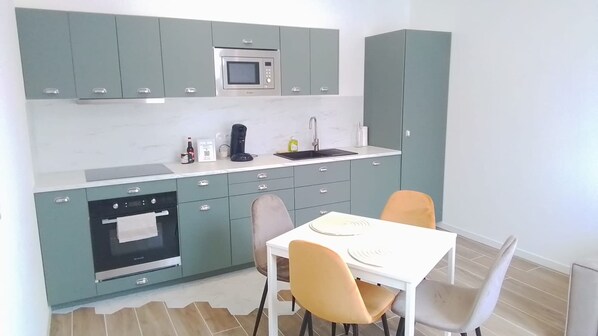 A compact kitchen with a microwave, oven, and sink, a dining table with chairs, and a small countertop with a coffee maker and other items.