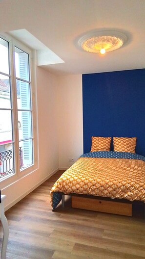 A bedroom with a bed, a window with shutters, and a blue accent wall.