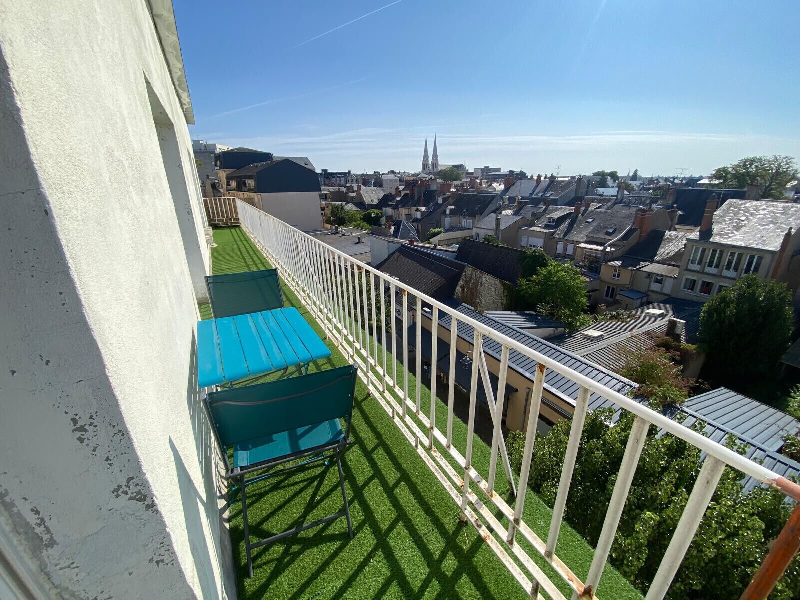A balcony with a view of a town, including a church spire, and a green lawn.