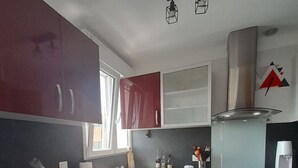 A modern kitchen with red cabinets, a stainless steel oven, and a black countertop. - T3 city centre- elevator- parking- panoramic view (Châteauroux)