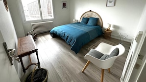 A bedroom with a bed, a chair, a table, a radiator, and a window. - T3 city centre- elevator- parking- panoramic view (Châteauroux)