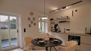 A modern dining area with a round table, white chairs, and a black tablecloth. There are shelves above the table with various items. - Mosel-Herz Trier vacation home! Directly on the Moselle, 10 min to the city center  (Trier)