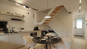 A modern kitchen with white cabinetry, a dining area with a round table and white chairs, and a staircase with wooden steps. - Mosel-Herz Trier vacation home! Directly on the Moselle, 10 min to the city center  (Trier)