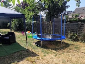 Ein Trampolin in einem Garten mit Zelt, Stühlen und einem kleinen Tisch mit Obst.