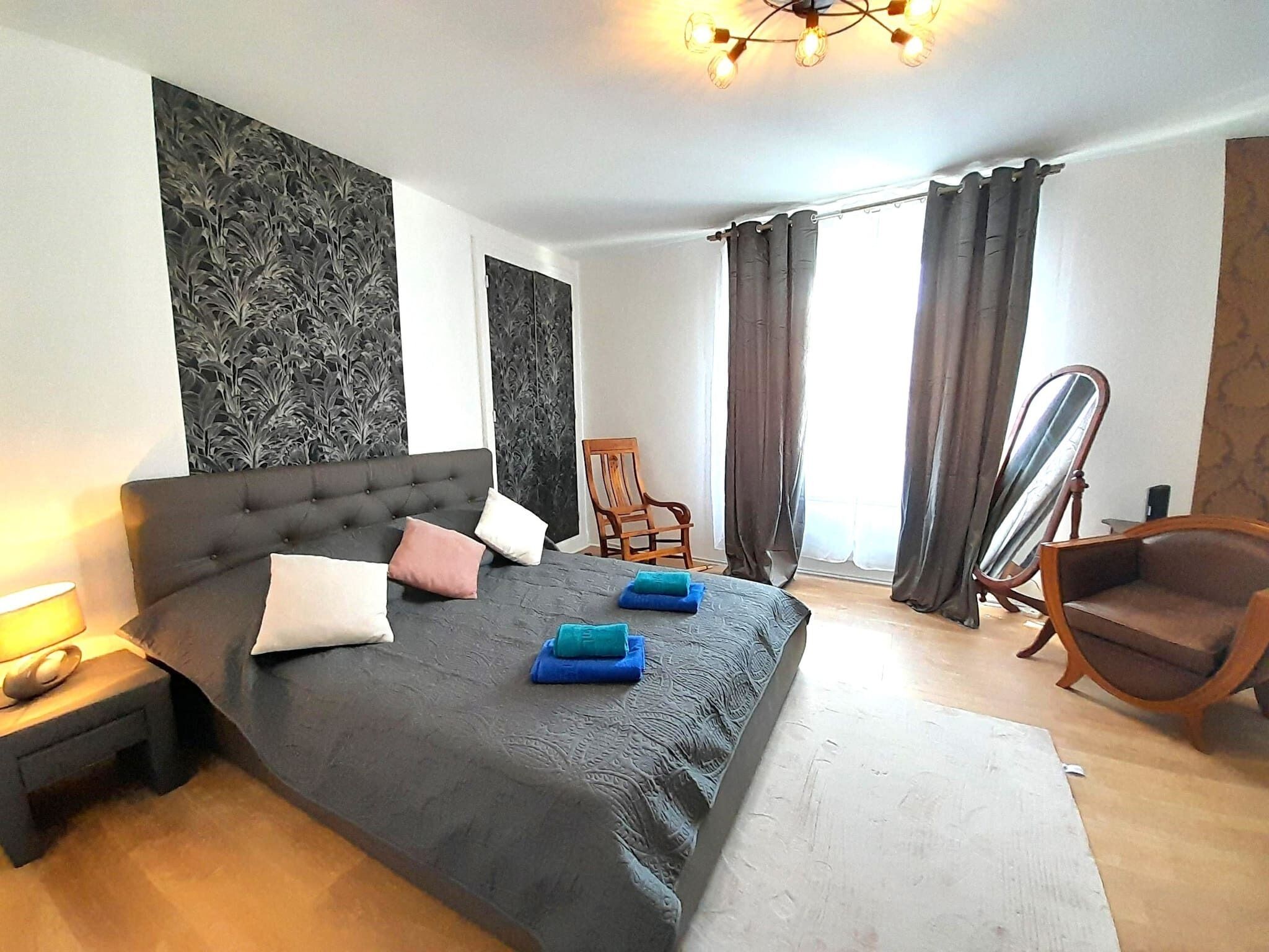 A bedroom with a large bed, a chair, a mirror, and a nightstand.