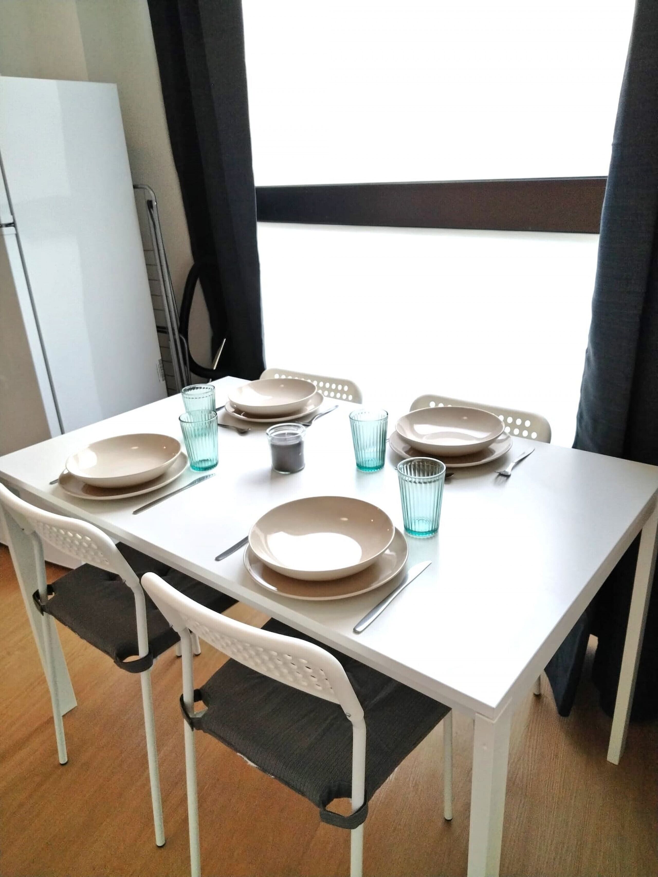 A dining table set with plates, glasses, and cutlery, surrounded by chairs.