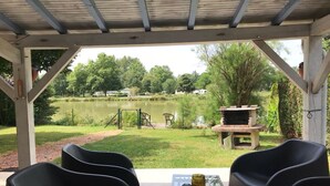 Un porche cubierto con vistas a un lago, mobiliario exterior y zona de barbacoa.