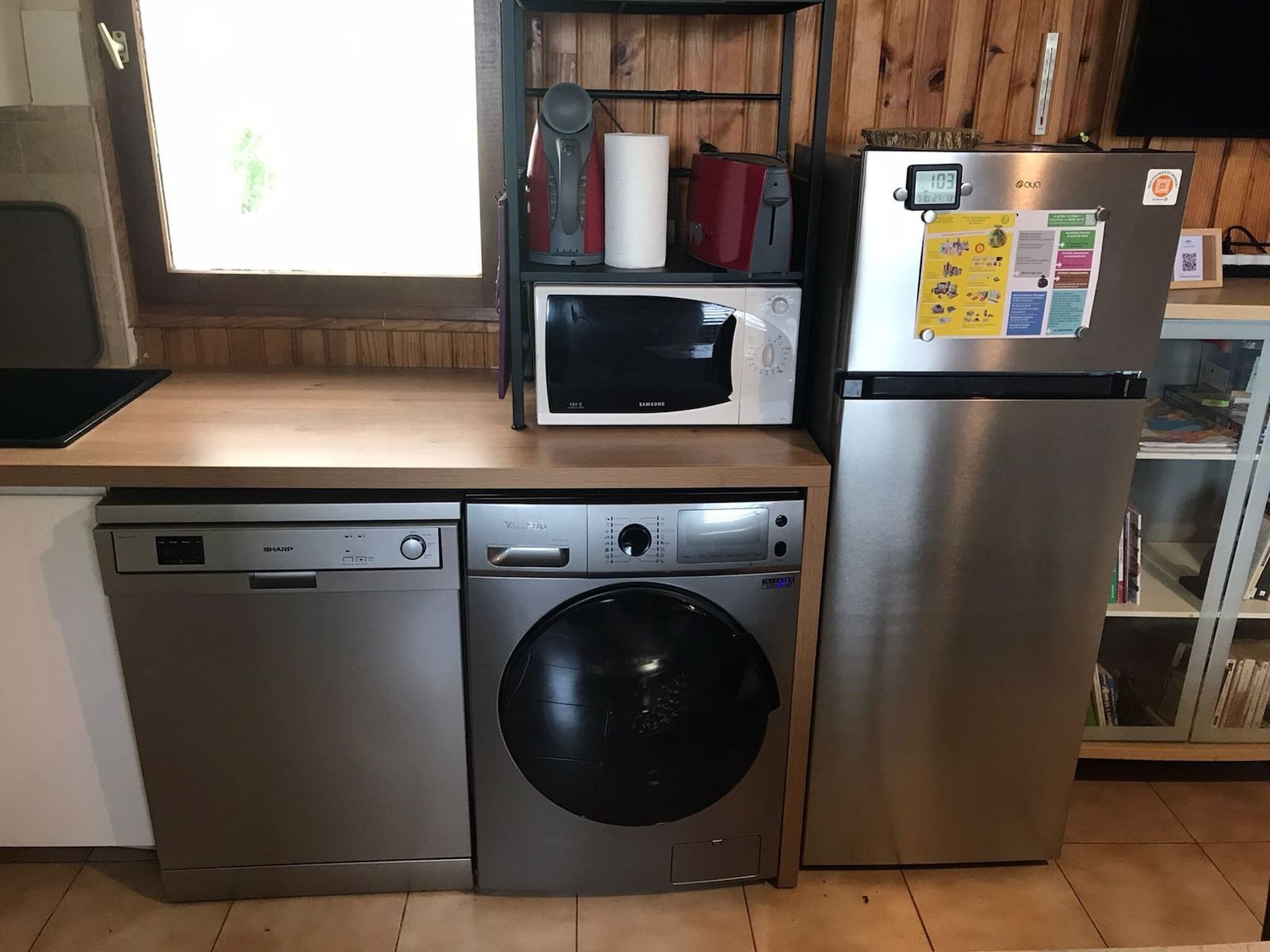 A compact kitchen with a dishwasher, washing machine, microwave, and refrigerator.