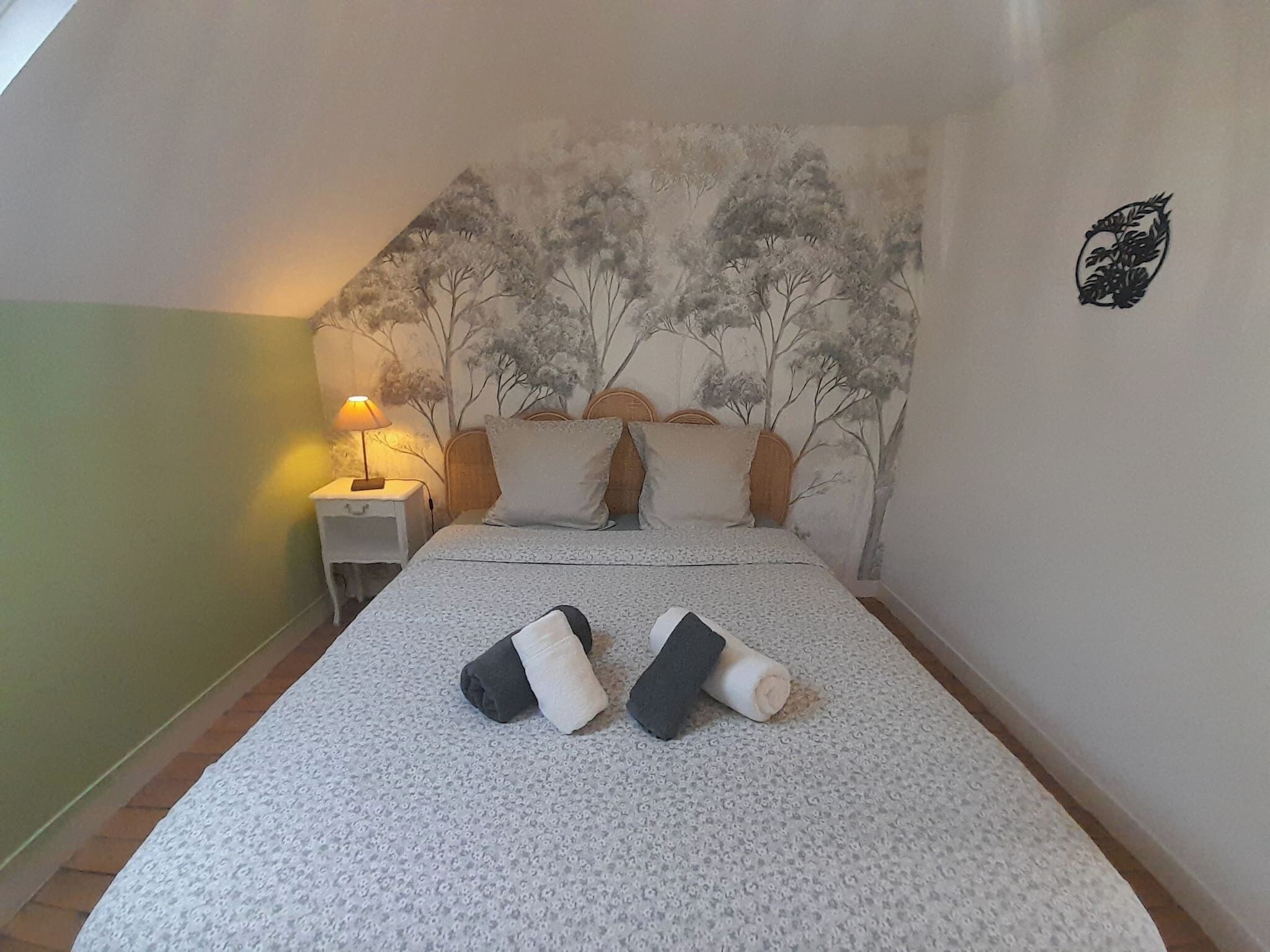 A bedroom with a bed, a nightstand, a lamp, and a wall mural.
