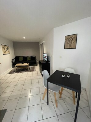 A modern living room with a sofa, coffee table, and a TV. There is a dining area with a table and chairs.