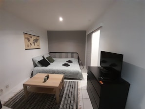 A small, neatly arranged bedroom with a single bed, a wooden side table, a television, and a world map on the wall.