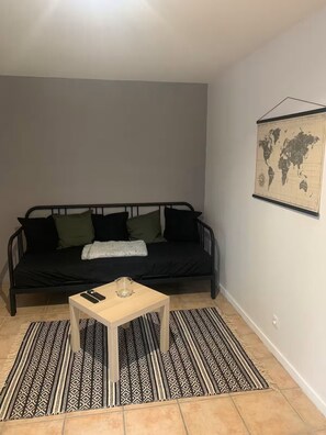 A small, cozy room with a black sofa, a wooden coffee table, and a patterned rug.