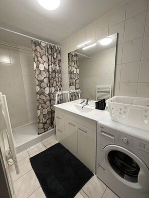 Une salle de bain moderne avec un rideau de douche à motifs de pierre, un lavabo encastré, un miroir, un radiateur blanc et un lave-linge à chargement frontal.