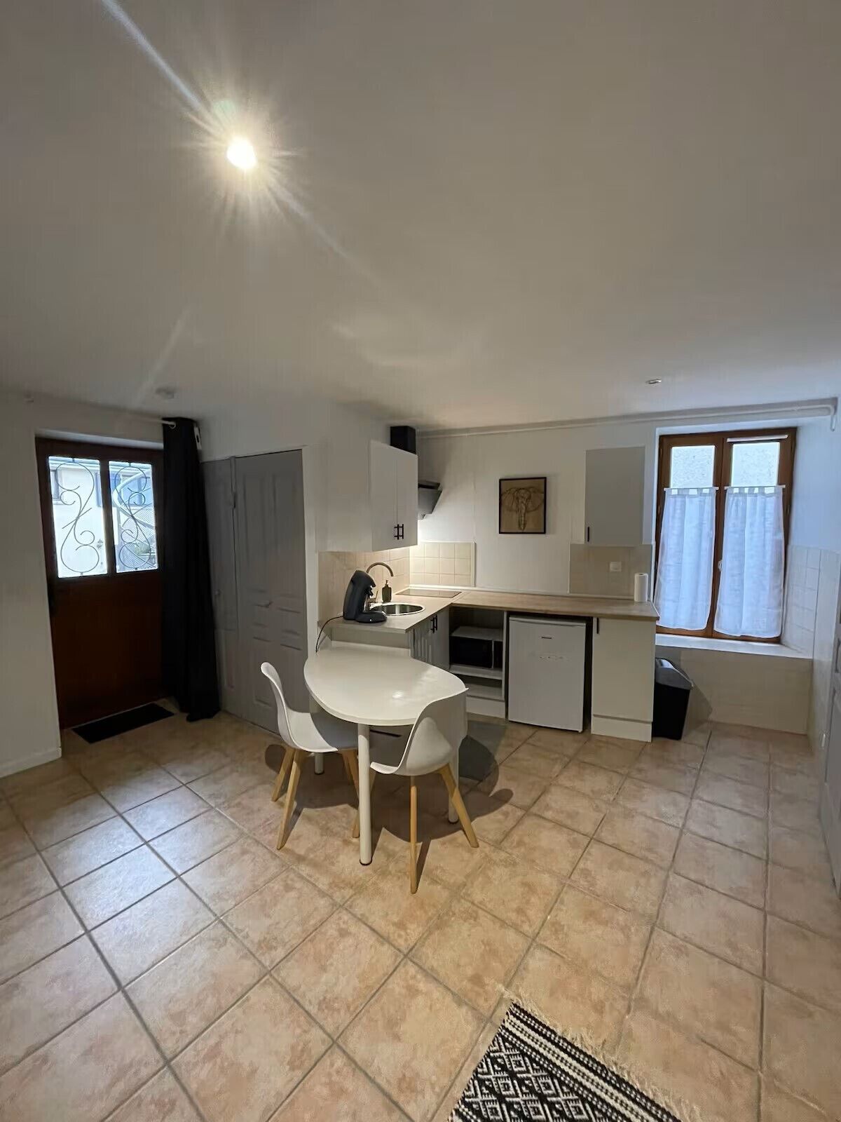 Una cocina compacta con comedor, un refrigerador pequeño y una ventana con cortinas.