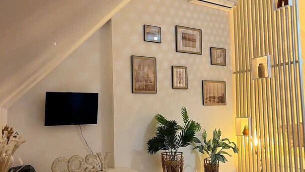 Ein modernes Wohnzimmer mit schrägverdeckter Decke, einem an der Wand montierten Flachbildfernseher, einem weißen Konsolentisch und zwei Zimmerpflanzen.
