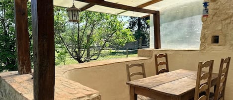 Un porche cubierto con una mesa y sillas de madera, un farol colgante y vistas a la vegetación.