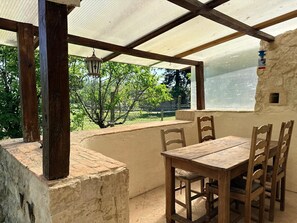 Un porche cubierto con una mesa y sillas de madera, un farol colgante y vistas a la vegetación.