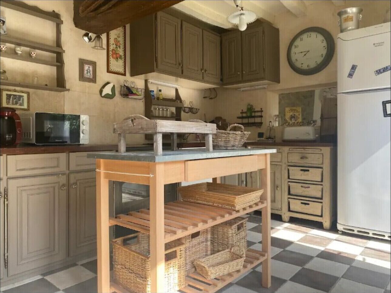 Une cuisine avec des meubles de rangement en bois, un four à micro-ondes, un réfrigérateur et une table avec des paniers.