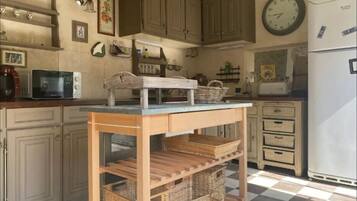 Une cuisine avec des meubles de rangement en bois, un four à micro-ondes, un réfrigérateur et une table avec des paniers.