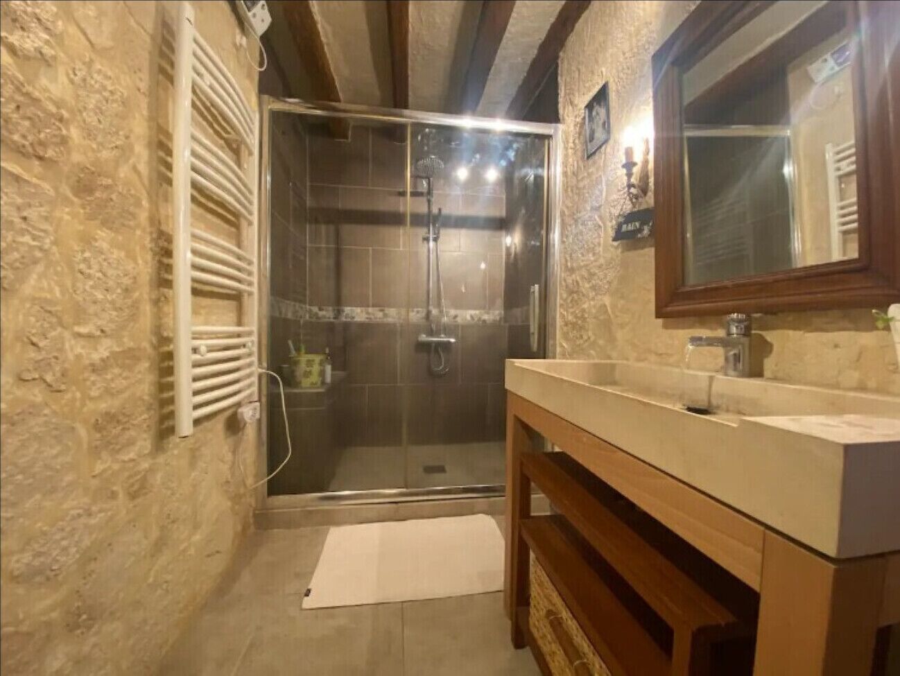 Une salle de bain dotée d’une douche à parois de verre, d’un meuble-lavabo en bois et d’un mur en pierre.