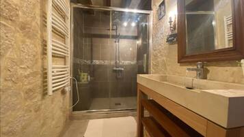 Une salle de bain dotée d’une douche à parois de verre, d’un meuble-lavabo en bois et d’un mur en pierre.