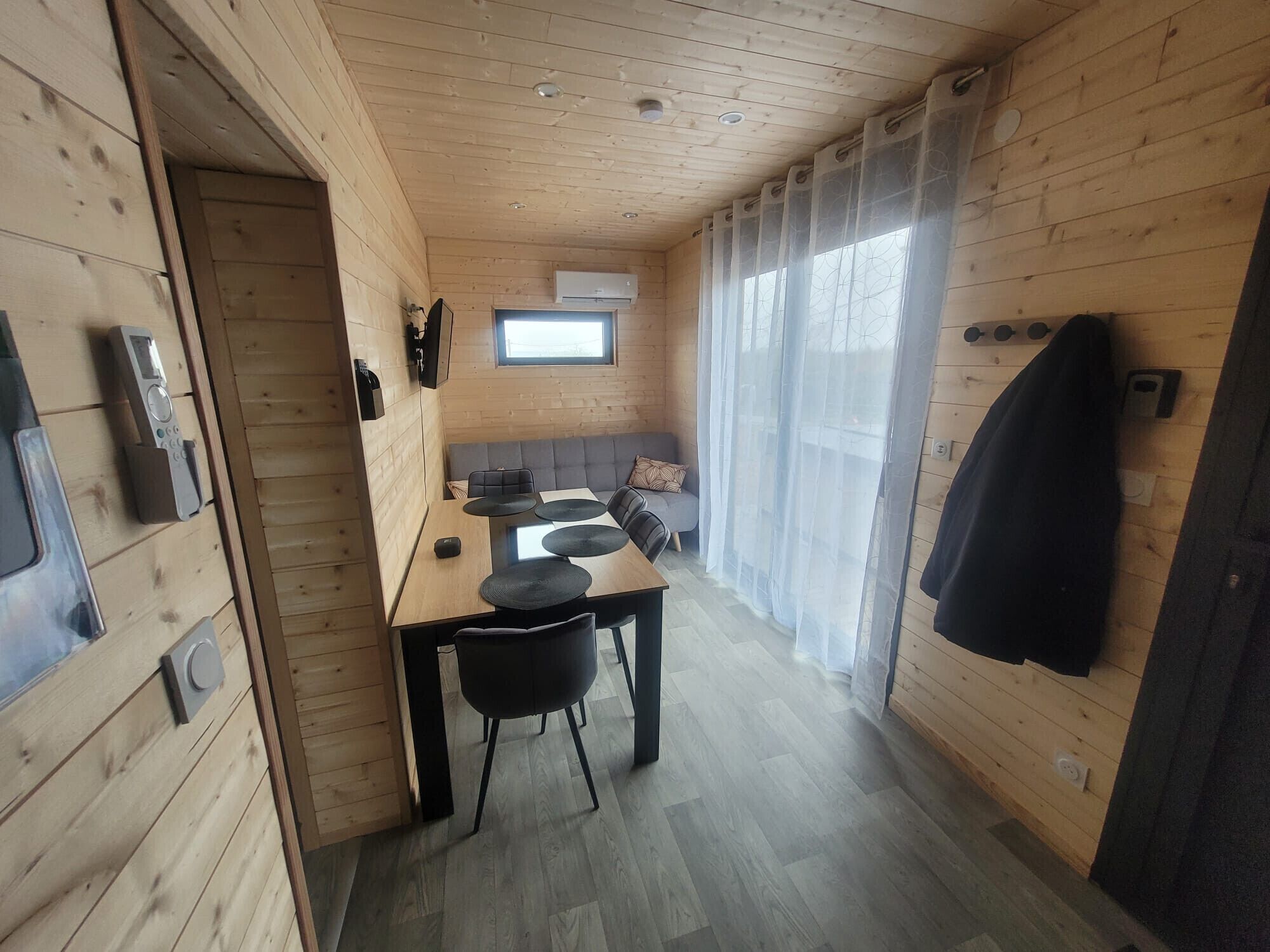 Une cabane en bois comprenant un coin repas, une petite cuisine et une fenêtre avec des rideaux.