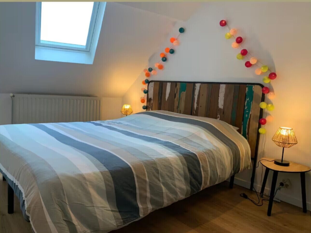 A bedroom with a bed, a skylight, a wall-mounted lamp, and a decorative string of balls.