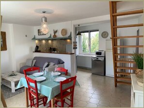 A dining area with a table set for four, a kitchen in the background, and a wooden ladder. - Maison proche du lac-4 pers-wifi-cour (Châteauroux)