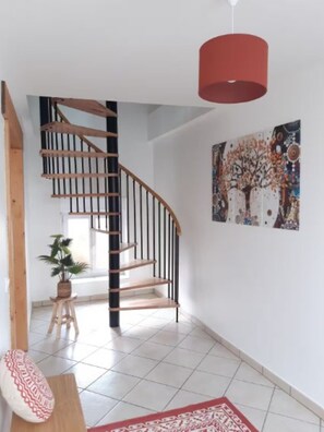 A modern interior with a spiral staircase, a red pendant light, a patterned rug, and a wall with a tree painting.