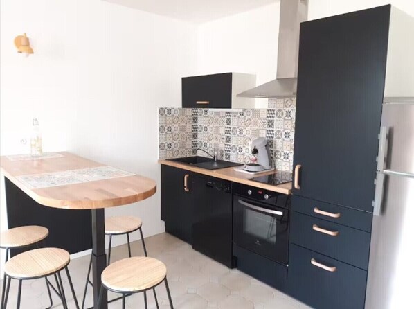 A compact kitchen with a wooden table and stools, black cabinets, and a tiled backsplash.