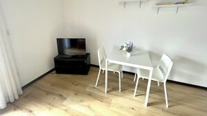Een kleine eethoek met een witte tafel en stoelen, een zwarte kast en een wandplank met boeken.