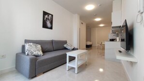 A modern living room with a grey sofa, a white coffee table, and a flat-screen TV mounted on the wall.