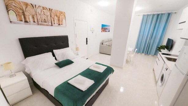 A modern hotel room with a large bed, a bedside table, a desk, and a washing machine.