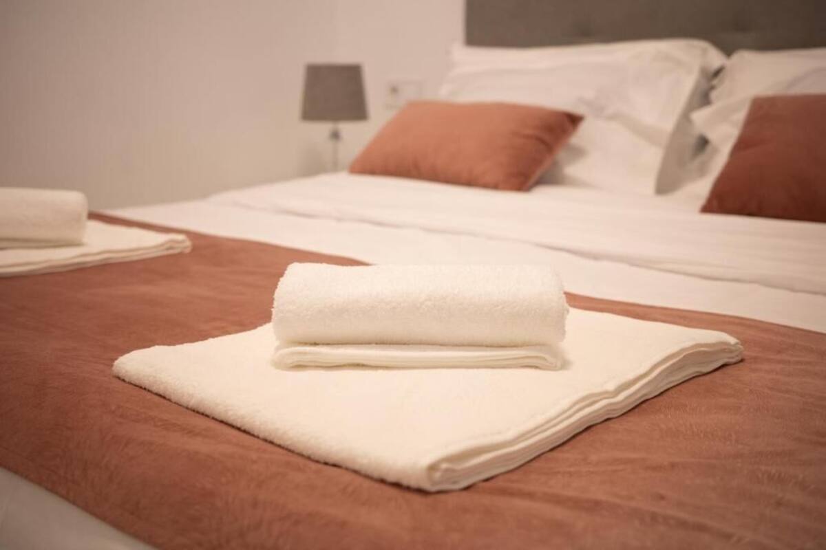 A neatly made bed with white linens and a folded white towel on a brown bedspread.