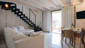 Una sala de estar moderna con un sofá blanco, una mesa de comedor de cristal y una escalera negra.