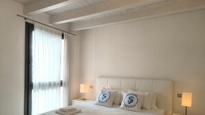 Habitación de hotel con una cama grande, dos almohadas con logotipos, una mesita de noche con lámpara y una ventana con cortinas.