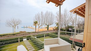 Un balcón con vista a una playa y un puente, amueblado con un sofá blanco y una mesita.