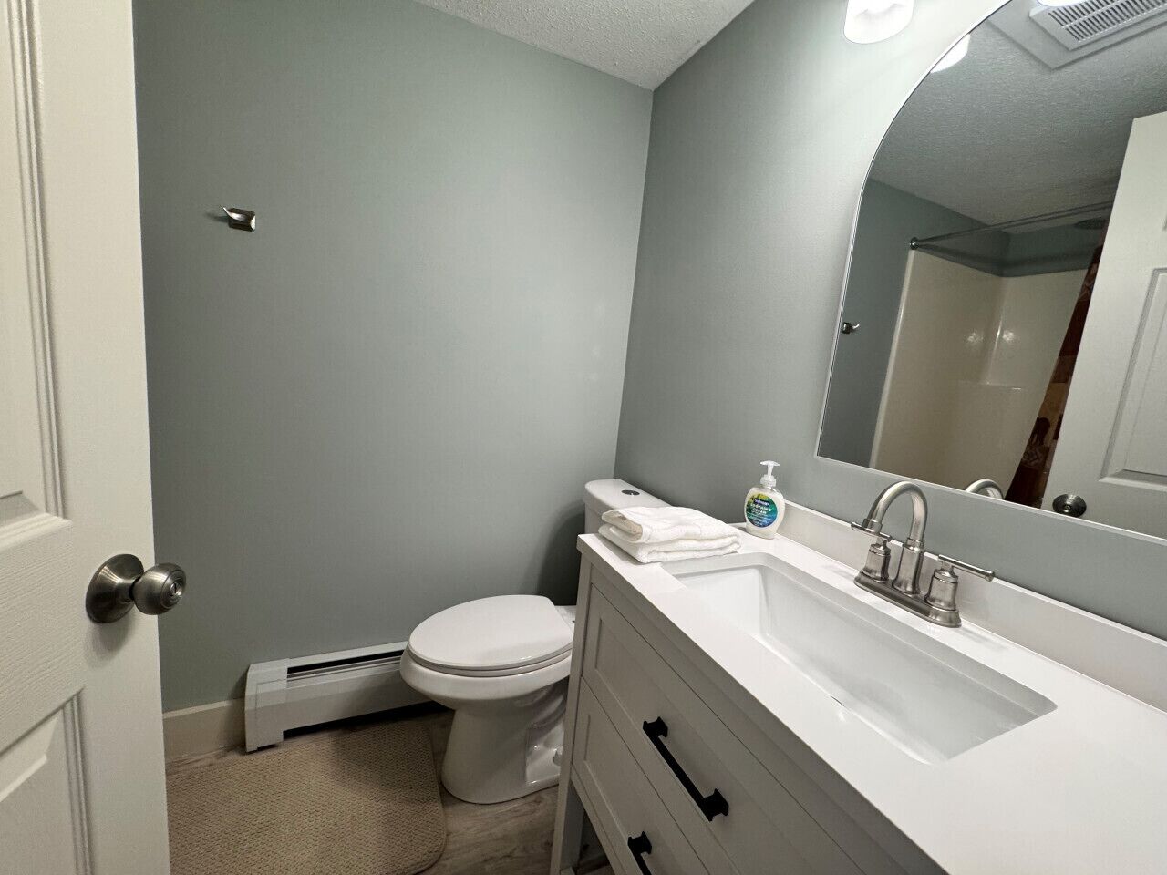 A bathroom with a toilet, a white sink, a mirror, and a towel on the sink.