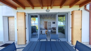 Une terrasse couverte avec une table et des chaises, des portes-fenêtres coulissantes donnant sur un espace intérieur comprenant un canapé et un coin repas.