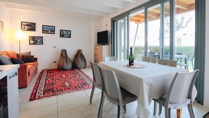 Un salon moderne comprenant un canapé, une table à manger avec des chaises, un tapis rouge à motifs et une grande fenêtre donnant sur l’extérieur.