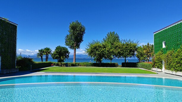 Une piscine à l’eau d’un bleu cristallin, entourée d’une végétation luxuriante et bien entretenue, avec vue sur la mer.