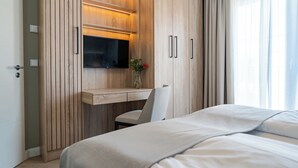 A hotel room with a bed, a desk with a chair, a TV mounted on the wall, and a window with curtains.