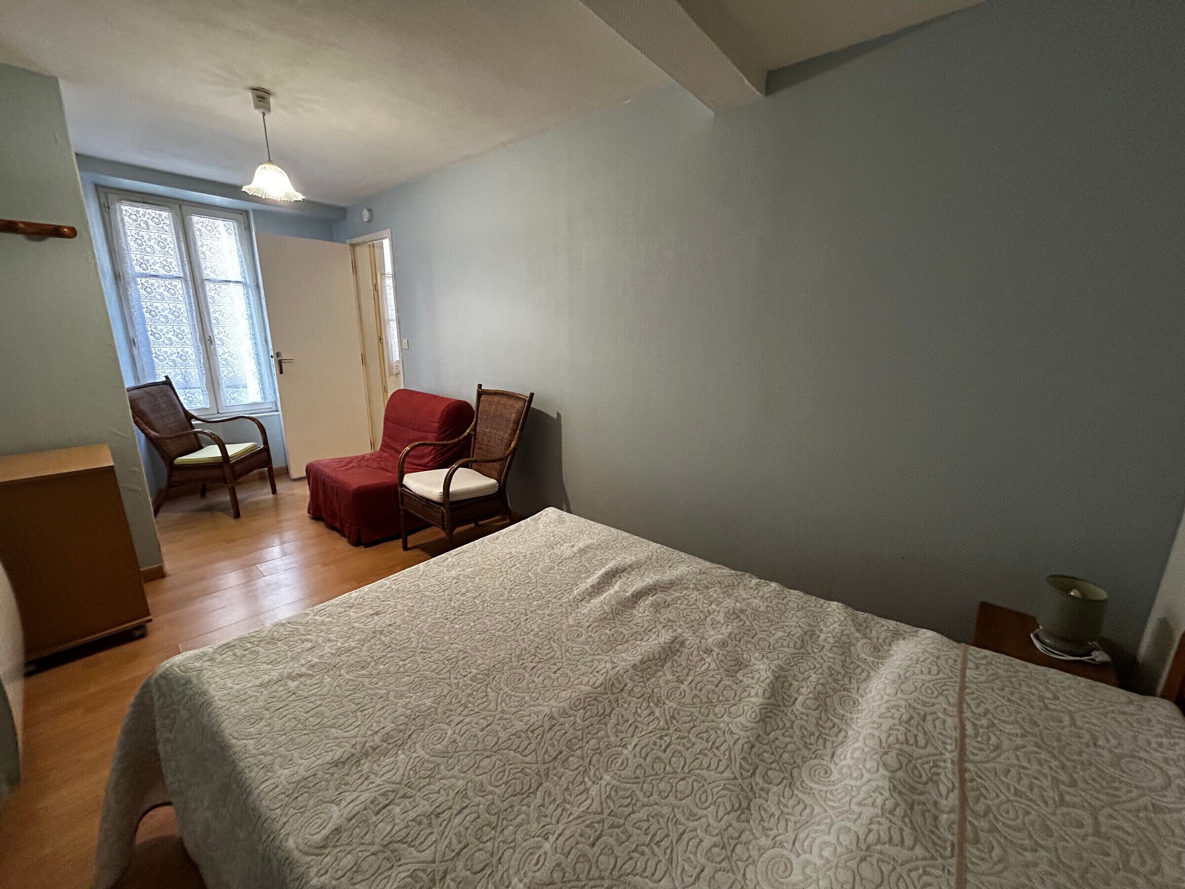 A bedroom with a bed, a wooden chair, a red chair, and a desk.