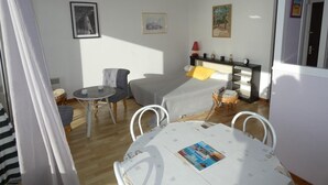 A compact room with a bed, a small table, and a chair. There are wall-mounted shelves with items on them. - Seaside Studio in Notre-Dame-de-Monts - Pets allowed, Parking (Notre-Dame-de-Monts)