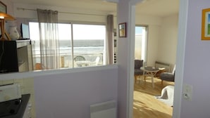 A room with a large window overlooking the ocean, a kitchenette, and a seating area with a view. - Seaside Studio in Notre-Dame-de-Monts - Pets allowed, Parking (Notre-Dame-de-Monts)