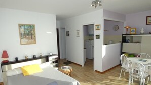 A room with a bed, a desk, a chair, a dining table with chairs, a kitchen area, and a living area with a sofa. - Seaside Studio in Notre-Dame-de-Monts - Pets allowed, Parking (Notre-Dame-de-Monts)