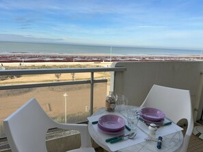 Un balcó amb taula preparada per a dues persones, amb vista a una platja amb vegetació vermella i cel serè.