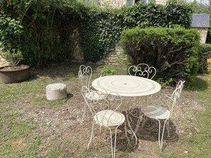 Une table ronde en métal, entourée de quatre chaises, et le tout est bordé par un mur de pierres et de la verdure.